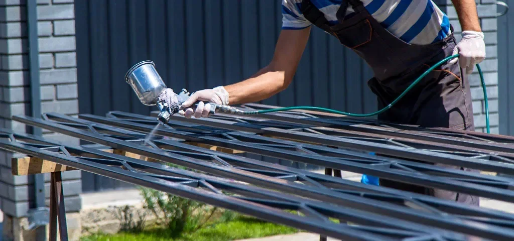 mężczyzna malujący pistoletem metalowe elementy ogrodzenia